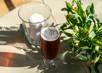 Cold dark beer on restaurant table, craft porter beer, ale froth pint glass in garden on a sunny summer day