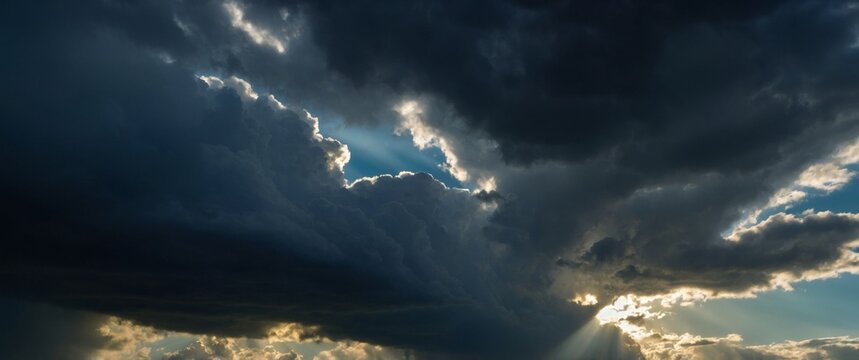 Dramatic sky with rays of light piercing through dark clouds evoking a sense of awe and the sublime beauty of nature.