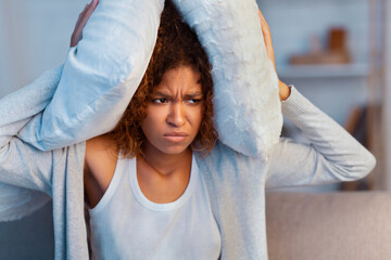 Annoyed woman covering ears with pillow, suffering from noisy neighbours