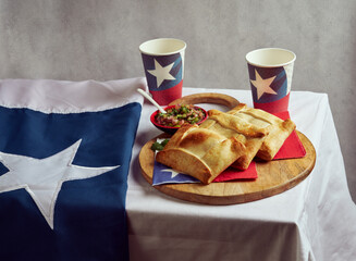 Still life of Chilean Empanadas de Pino and Pebre on a wooden tray and glasses with the Chilean...