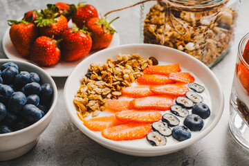 A light and healthy berry breakfast: nranola with strawberries, blueberries and Greek yogurt in a white bowl on a gray background. Selected focus.
