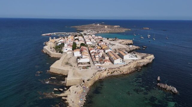 Aerial filming of Spanish island Tabarca. Sunny day, blue water surrounds, yachts in the bay. Calm sea, bustling city and beach. Tourist hotspot on Costa Brava.