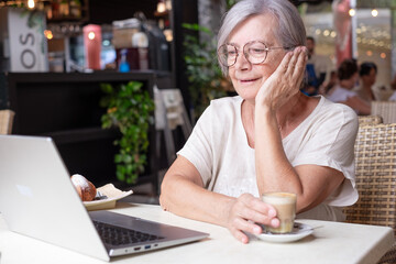 Attractive senior woman sitting in a cafe using laptop while enjoying a breakfast with pastry and...