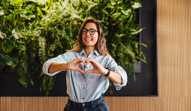 Business woman doing a heart gesture as she stands in a sustainable business office