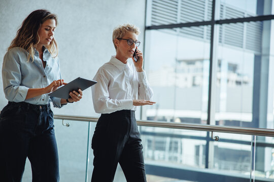 Morning briefings: Executive assistant walks behind her boss in a busy business office - Powered by Adobe