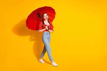 Photo portrait of young beautiful positive girl wearing red top and jeans strolling romantic with parasol isolated on yellow color background © deagreez