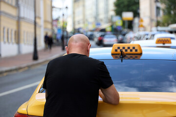 Bald man in black t shirt standing on city street near the trunk of taxi car © Oleg