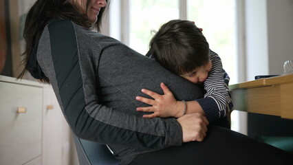 Pregnant woman with her young child embracing her belly, capturing a candid and tender moment of...