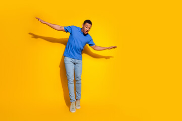 Full size photo of pretty young male keep balance look down empty space wear trendy blue outfit isolated on yellow color background