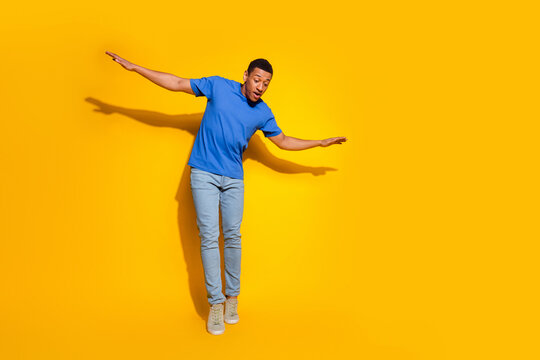 Full size photo of pretty young male keep balance look down empty space wear trendy blue outfit isolated on yellow color background