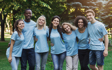 Group of happy young diverse volunteers embracing at park, ready for work, copy space