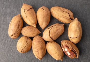 Several unshelled pecan nuts on slate stone, macro, top view.