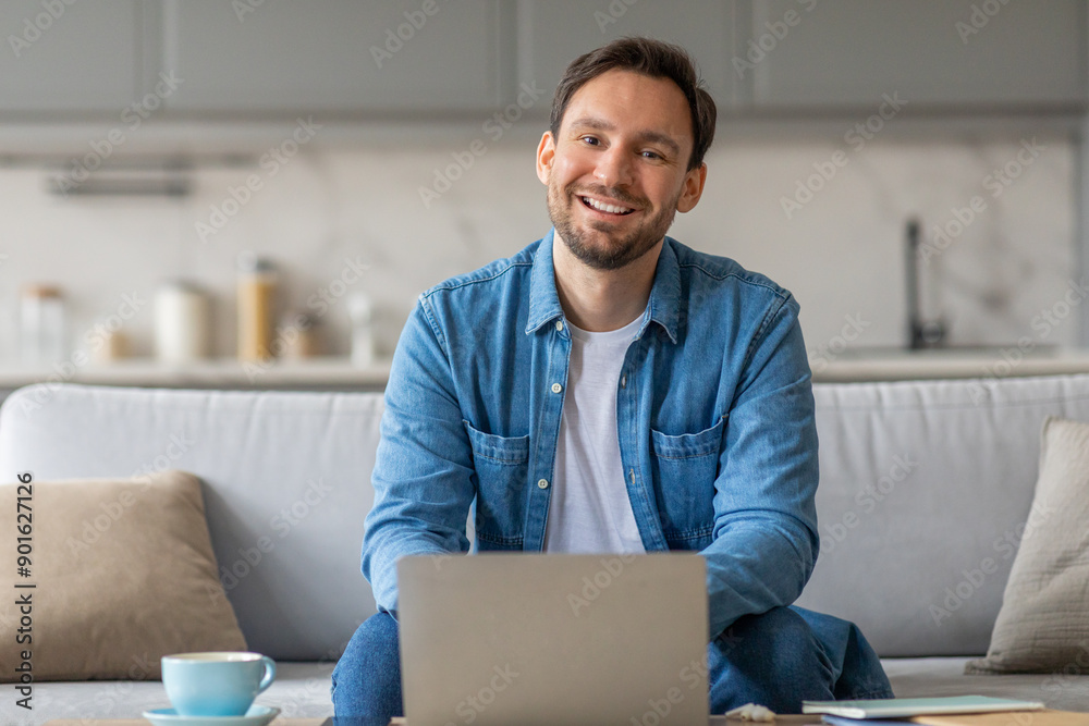 Aufkleber a man is sitting on a couch in his living room, smiling and looking at the camera while using his la