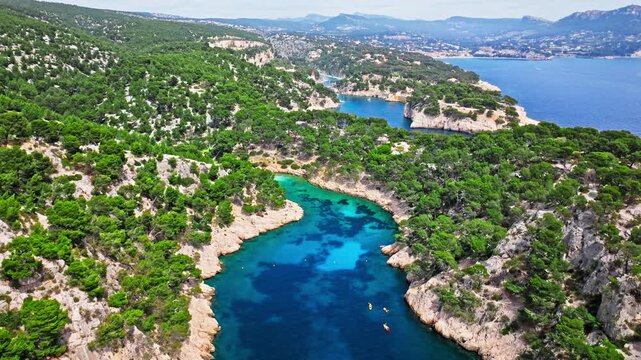 Aerial view of Tourist attraction beach, people enjoying summer vacation in Parc du Mugel, France. Snug Cove framed by rugged cliffs, with calm swimming off a pebble beach, and turquoise clear water.