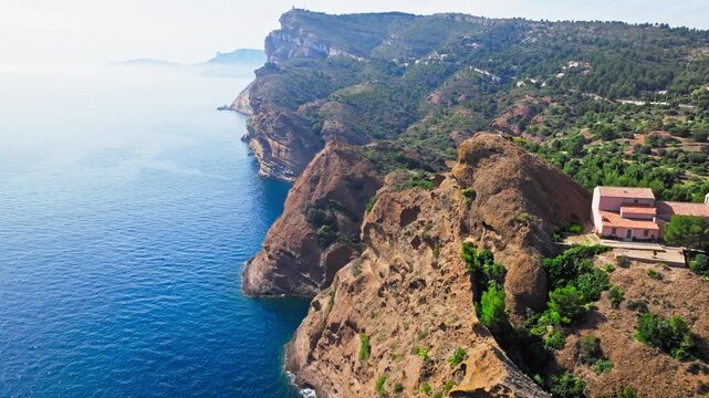 Aerial view of a Botanical garden with Snug Cove framed by rugged cliffs in Parc du Mugel. View from above of swimming off a pebble beach with turquoise clear water in France.