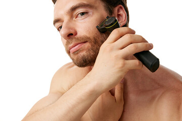 Shirtless man trimming his beard with electric trimmer, highlighting importance of grooming tools in modern male beauty routines, isolated on white background. Concept of beauty, skin care, cosmetics