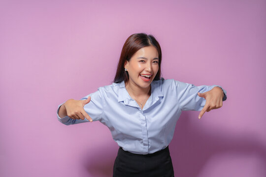 Asian businesswoman with a wide smile pointing down with both index fingers against a vibrant purple background