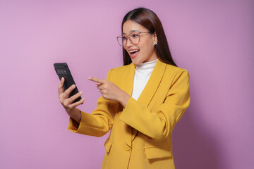 Naklejka premium Excited businesswoman wearing a yellow blazer is pointing at her mobile phone screen with a surprised look on her face