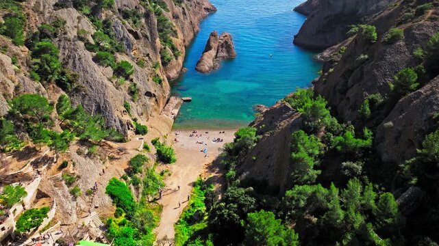 Aerial view of Tourist attraction beach, people enjoying summer vacation in Parc du Mugel, France. Snug Cove framed by rugged cliffs, with calm swimming off a pebble beach, and turquoise clear water.