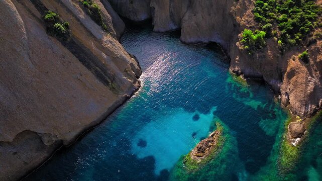 Aerial view of a Botanical garden with Snug Cove framed by rugged cliffs in Parc du Mugel. View from above of swimming off a pebble beach with turquoise clear water in France.