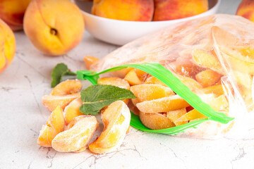 Frozen peaches in freezing bags with fresh ripe raw peach fruits on kitchen white table, Healthy simple canning, freezing stock up of fruit harvest for winter concept. 