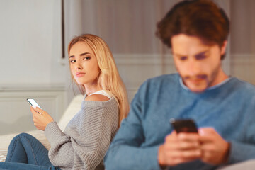 Cheating. Suspicious Wife Watching Husband Texting On Phone Suspecting Infidelity Sitting Indoor. Selective Focus