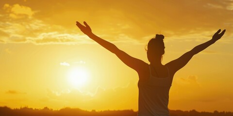 A woman is standing in the sun with her arms outstretched. The sun is setting in the background, creating a warm and peaceful atmosphere