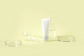Cosmetic tube surrounded by laboratory glassware, including beakers and petri dishes, on a pastel yellow background, representing skincare formulation concept