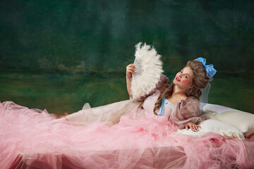 Portrait of beautiful young woman, royal person, princess in elegant dress lying on bed with...