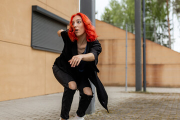 Happy positive emotional dancer curling in dance. Woman with red hair dancing on urban street, on...