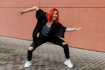 Happy positive dancer curling in dance. Woman with red hair dancing on urban street, on pink wall...