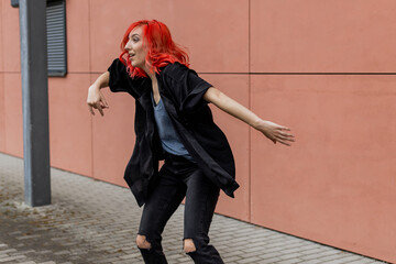 Happy positive dancer curling in dance. Woman with red hair dancing on urban street, on pink wall...