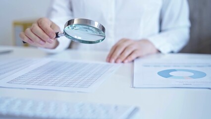 Businesswoman with white blues is analyzing financial data on a spreadsheet using a magnifying glass. Audit and taxes