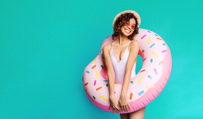 A smiling black woman is standing in front of a teal backdrop, holding a pink donut-shaped...