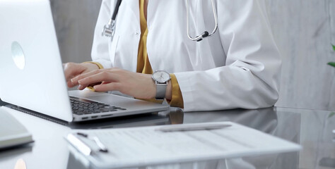 Doctor woman is using a laptop computer on a glass desk in medical office. Work place concept in Medicine