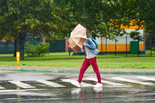 Man battles with an umbrella bending inward under the force of strong winds, man caught in downpour. Person navigating crosswalk in the rain suffers from strong wind. Motion blur effect, soft effect
