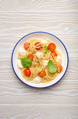 Delicious spaghetti with tomatoes and mozzarella cheese served on white wooden table with cutlery aside, top view