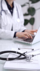 Stethoscope is lying on the glass table while doctor woman is working with laptop computer on the background. Medicine and pharmacy concept