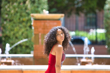 Obraz premium portrait beautiful young latin woman with big eyes and brunette with curly hair wearing a red dress walking among the trees in the park and making different facial expressions. Fashion concept.