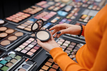 Woman holding face blush in her hands. Colorful eye shadows palettes and other male up products on...