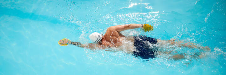 Banner. Swimmer with yellow paddle glides through pool, honing his freestyle technique under sun outdoor. Concept of professional sport, competition, active and healthy lifestyle. Ad