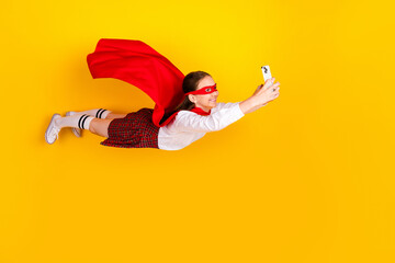 Full length photo of charming teenager pupil girl flying superhero hold device wear trendy uniform isolated on yellow color background
