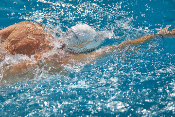 Close-up of swimmer in white cap cutting through sparkling blue water during intense training session at pool outdoor. Concept of professional sport, competition, active and healthy lifestyle. Ad