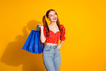 Photo portrait of pretty young girl hold shopping bags look empty space wear trendy red retro outfit isolated on yellow color background