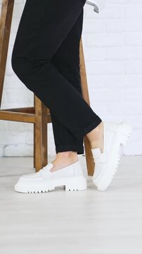 Fashionable white shoes presentation. Female model walks in fashionable footwear back and forth near the wooden tabouret. Vertical video