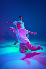 Talented young man and woman in casual sports clothes dancing hip-hop against purple studio background in neon light. Dance show. Concept of contemporary dance, hobby, youth