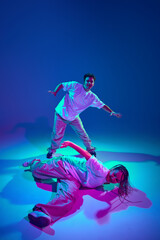 Young guy and girl in casual clothes dancing contemp, performing hip-hop against purple studio background in neon light. Concept of contemporary dance, hobby, youth