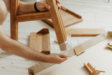 Man hands removing protective polythene film from new wooden furniture leg
