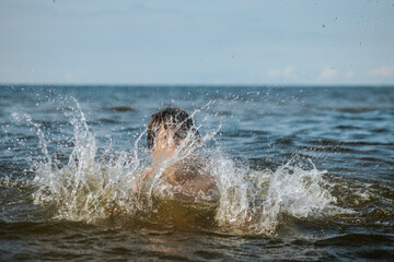 Fototapeta premium A young child struggling and shouting in the water, appearing to be in distress, with splashes around him and a vast expanse of water in the background. The scene evokes a sense of urgency and concern