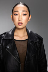 Fashion asian woman in black leather jacket posing against gray background portrait of stylish...
